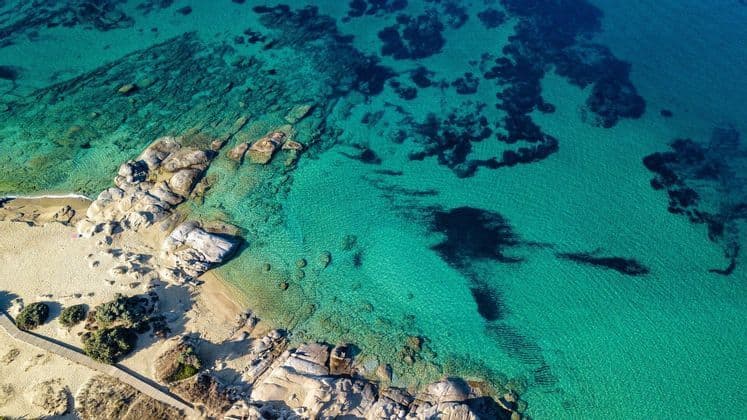 Una vista aerea di una costa rocciosa con una spiaggia sabbiosa, delimitata da acque marine limpide e turchesi.