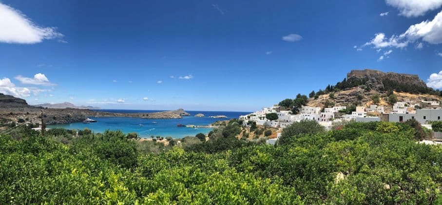 Un villaggio imbiancato a calce e un'acropoli su un pendio che domina una baia turchese, con alberi verdi in primo piano.