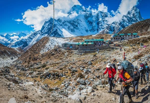 Un viaje en grupo de WeRoad haciendo senderismo por un sendero rocoso hacia un refugio de montaña, con grandes picos nevados de fondo.
