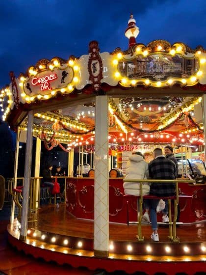 Un grupo WeRoad conversando en un bar dentro de un carrusel iluminado por la noche.