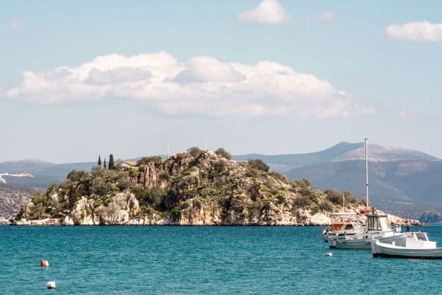 Barcos blancos flotan en aguas turquesas frente a una pequeña isla rocosa cubierta de vegetación bajo un cielo nublado.