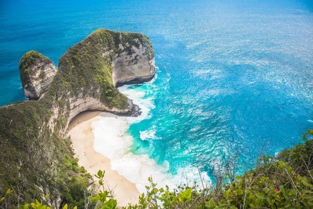 Una vista dall'alto di una scogliera ricoperta di verde che si protende in un oceano turchese, riparando una spiaggia isolata di sabbia bianca.