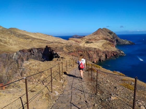Una donna di un viaggio di gruppo WeRoad cammina su un sentiero di pietra lungo una costa rocciosa che si affaccia sull'oceano.