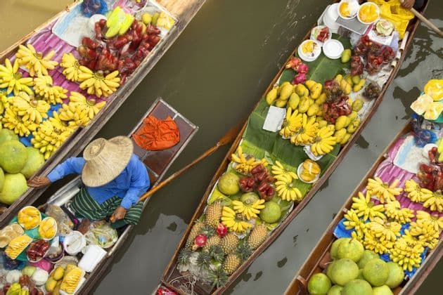 An overhead view of a floating market with boats laden with fresh, colorful tropical fruit, including bananas and pineapples.