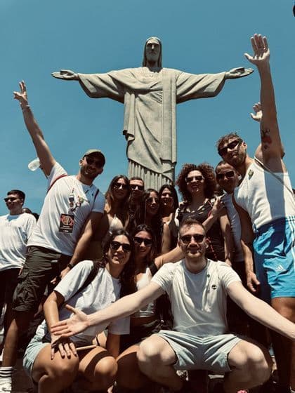 Un gruppo WeRoad in viaggio posa per una foto di gruppo davanti alla statua del Cristo Redentore sotto un cielo sereno.