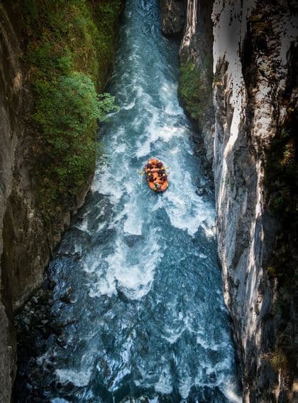 Vista aerea di un gruppo WeRoad che fa rafting su un gommone arancione, in un fiume impetuoso che attraversa un canyon profondo e stretto.