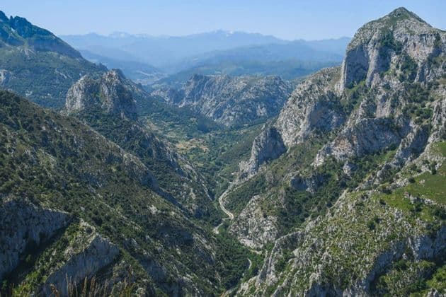 Una vista panorámica de un valle profundo que serpentea a través de una cadena montañosa escarpada y arbolada bajo un cielo azul claro.