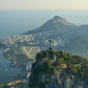Una vista aerea della statua del Cristo Redentore su una montagna, che domina una città costiera con una grande laguna e l'oceano.
