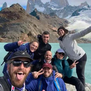 Un grupo de WeRoad se toma una selfie sonriente junto a un lago turquesa con montañas nevadas de fondo.
