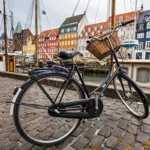 Un vélo noir avec un panier en osier est garé dans une rue pavée le long d'un canal avec des bateaux et des bâtiments colorés.