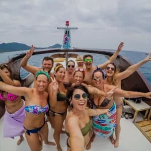 Un voyage de groupe WeRoad avec des personnes en maillot de bain posant pour un selfie sur le pont d'un bateau en mer.