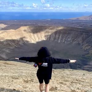 Un accompagnatore WeRoad sta con le braccia aperte sul bordo di un grande cratere vulcanico, affacciato sul mare.