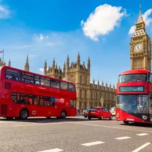 Deux bus rouges à impériale sur une rue avec les Chambres du Parlement et Big Ben en arrière-plan sous un ciel bleu.