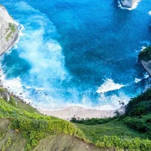 An aerial view of a secluded sandy beach in a cove, with turquoise waves crashing between steep, green cliffs.