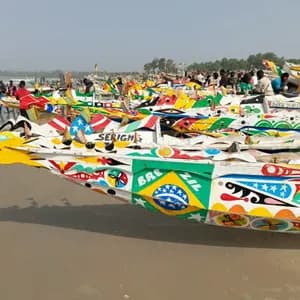 Una flota de barcos de pesca de madera intrincadamente pintados descansando en una playa de arena con gente reunida al fondo.