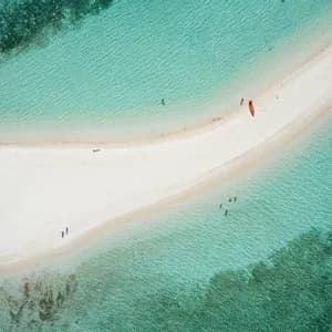 Una vista aerea di una lingua di sabbia bianca in acqua turchese, dove persone nuotano vicino a un kayak e una barca a bilanciere ormeggiata.