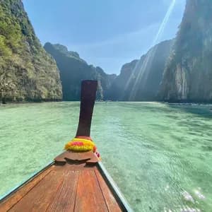 Una vista dalla prua di una barca tradizionale a coda lunga in legno che solca acque cristalline color turchese in una laguna circondata da alte scogliere verdi.