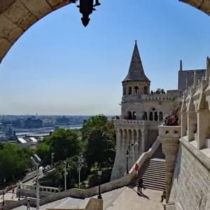 Ein Blick durch einen Steinbogen auf eine historische Bastei mit spitzem Türmchen, die eine Stadtkulisse und einen Fluss an einem sonnigen Tag überblickt.
