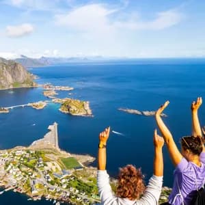 Due persone in viaggio di gruppo WeRoad con le braccia alzate, che ammirano un villaggio costiero da una scogliera.