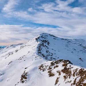 Una cima montuosa innevata con una cresta rocciosa sotto un cielo blu con nuvole sparse.