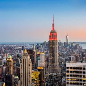 Una vista aérea del horizonte de la ciudad de Nueva York al anochecer, con el Empire State Building iluminado en rojo contra un cielo degradado.