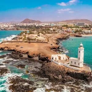Vista aerea di un faro bianco su una penisola rocciosa vicino a una città costiera con acqua turchese