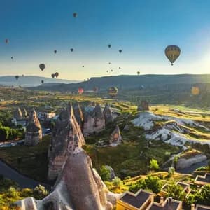 Dutzende Heißluftballons schweben bei Sonnenaufgang über einem Tal mit einzigartigen Felsformationen und einem Dorf.