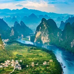 Une vue aérienne d'une rivière sinuant à travers une vallée de montagnes karstiques verdoyantes, avec de petits villages et des champs sur les rives.