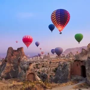 Mongolfiere colorate sorvolano un paesaggio di formazioni rocciose uniche e abitazioni rupestri durante un'alba dai colori pastello.