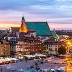 Una vista elevada de una plaza histórica de ciudad europea con edificios coloridos y una catedral, iluminada al atardecer.