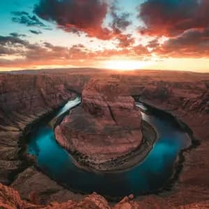 Un'ampia vista di un fiume che si snoda in un canyon di roccia rossa sotto un cielo al tramonto colorato.