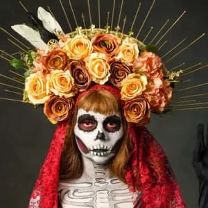 Una persona in costume da Giorno dei Morti, con trucco da calavera e un elaborato copricapo floreale con punte dorate.