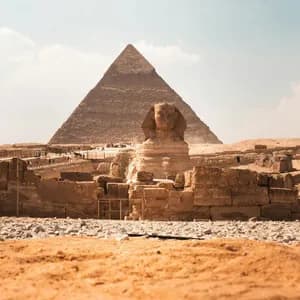 Una vista desde el suelo de la Gran Esfinge con una gran pirámide al fondo, rodeada de antiguas ruinas de piedra bajo un cielo brillante.