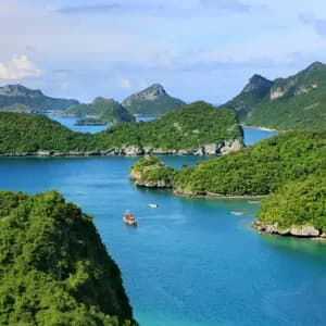 Una vista aerea di un arcipelago con isole verdi e lussureggianti, acqua blu calma e diverse piccole barche che navigano.