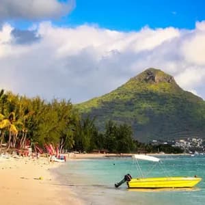 Un bateau à moteur jaune repose dans l'eau turquoise d'une plage de sable bordée de palmiers, avec une grande montagne verte en arrière-plan.