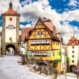 Coloridos edificios de entramado de madera y un campanario bordean una calle empedrada serpenteante bajo un cielo parcialmente nublado.