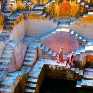 Deux femmes en tenue traditionnelle descendent les escaliers géométriques en pierre d'un ancien puits à degrés.
