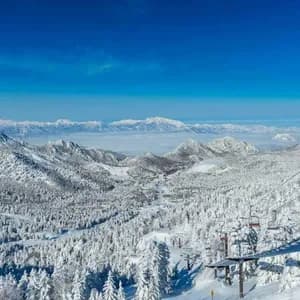 Una vista panoramica da una seggiovia mostra una vasta catena di montagne e foreste innevate sotto un cielo azzurro brillante.