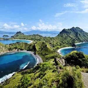 Eine Vogelperspektive auf schroffe grüne Inseln mit Sandbuchten, wo zwei Personen auf einem Grat den türkisfarbenen Ozean überblicken.