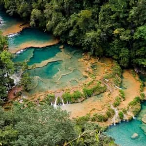 Eine Luftaufnahme von gestuften türkisfarbenen Wasserbecken und Wasserfällen, die durch einen dichten grünen Wald fließen.