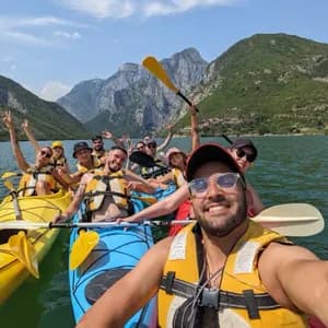 Un viaje en grupo de WeRoad se toma una selfie sonriente mientras hacen kayak en un lago con montañas verdes de fondo.