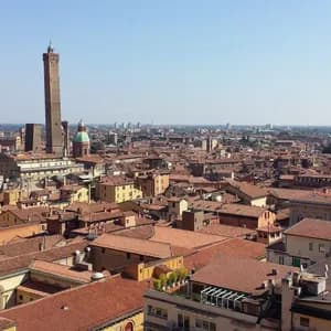 Una vista panoramica di una città con tetti di tegole rosse, un'alta torre di mattoni e una cupola prominente sotto un cielo sereno.