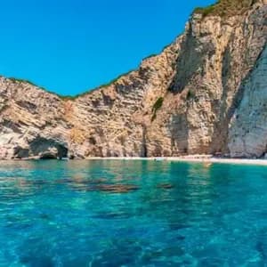 Una grande scogliera rocciosa si erge su una spiaggia sabbiosa isolata e un mare limpido e turchese sotto un cielo blu.
