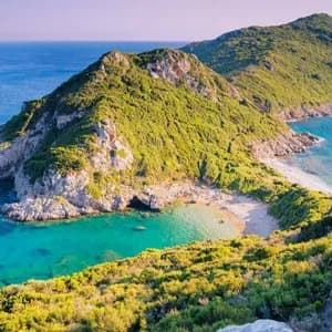A lush green, rocky headland forms a small cove with a sandy beach and clear, turquoise water on a sunny day.