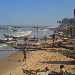 Ein belebter Sandstrand mit vielen Menschen und bunten hölzernen Fischerbooten am Ufer und in den sanften Wellen unter klarem Himmel.