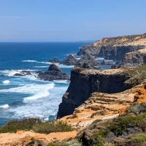 Eine zerklüftete Küste mit steilen Klippen und Felsnadeln, die unter klarem Himmel aus dem blauen Ozean ragen.