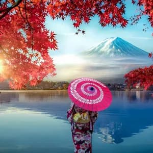 Una persona in kimono con un ombrellino rosa in riva a un lago, osserva una montagna innevata incorniciata da foglie autunnali rosse.