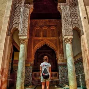 Una mujer con camiseta y mochila de WeRoad de pie mirando hacia un gran arco ornamentado con tallas detalladas y mosaicos de azulejos.