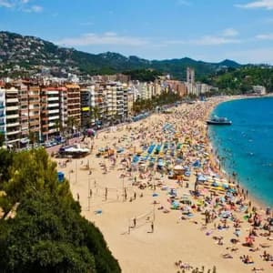 Una vista aerea di una spiaggia sabbiosa affollata accanto a una città costiera, con persone che prendono il sole e nuotano nell'oceano blu.