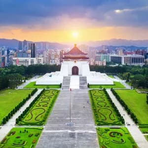 Una veduta aerea di una sala commemorativa bianca con un tetto blu, sullo sfondo di uno skyline moderno e montagne al tramonto.